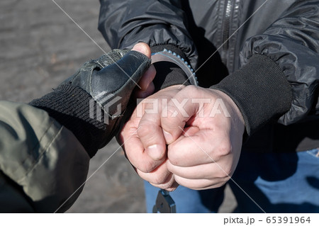 a police officer puts handcuffs on the hands of a bandit 65391964