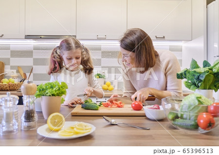 Mother and daughter cooking together in kitchen vegetable salad, parent and child are talking smiling. 65396513