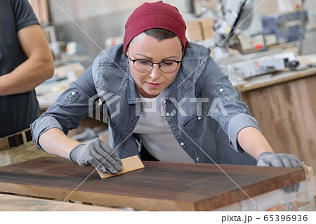 Mature craftswoman working in woodshop. Female painting wooden board with oil, varnish. 65396936