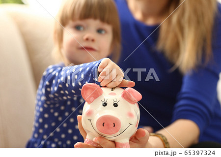 Child little girl arm putting coins into piggybank Child little girl arm putting coins into piggybank 65397324