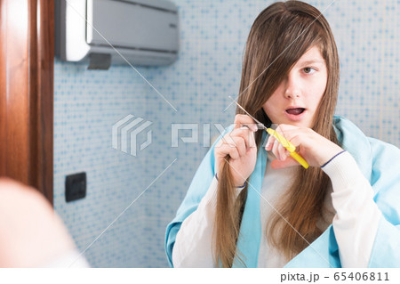A beautiful young girl is holding a scissor to cut her hair herself during lockdown of coronavirus A beautiful young girl is holding a scissor to cut her hair herself during lockdown of coronavirus 65406811
