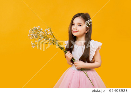 Cute young girl with wildflowers bouquet in hands on yellow background 65408923