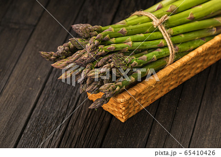 Bunch of fresh green asparagus spears in basket on a rustic wooden table. 65410426