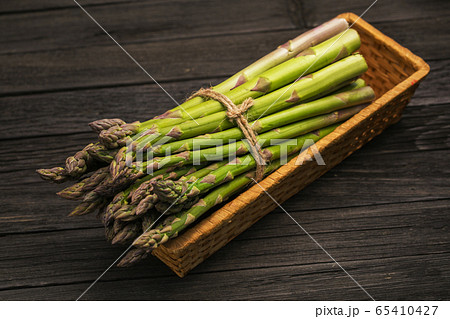 Bunch of fresh green asparagus spears in basket on a rustic wooden table. Bunch of fresh green asparagus spears in basket on a rustic wooden table. 65410427