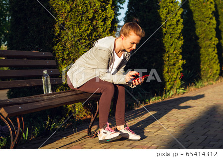 Young female runner, athlete resting after jogging in the city street in sunshine. Beautiful caucasian woman training, listening to music 65414312