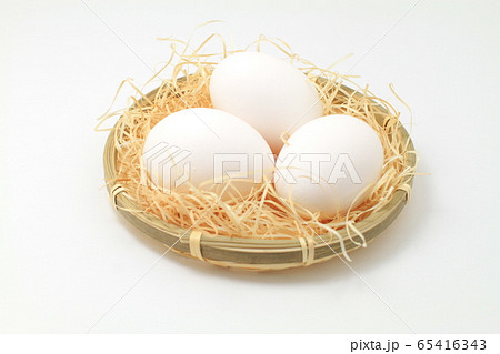 わらを敷いた小さいザル盛り白い鶏卵三個、白バック 65416343