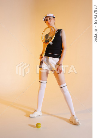Girl tennis player with a racket in sportswear and white sneakers on a yellow background in the Studio 65427927