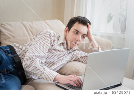 Young man lying on sofat and using laptop at home 65429072