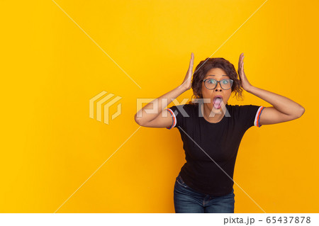 African-american beautiful young woman's portrait on yellow studio background, emotional and expressive. Copyspace for ad. African-american beautiful young woman's portrait on yellow studio background, emotional and expressive. Copyspace for ad. 65437878