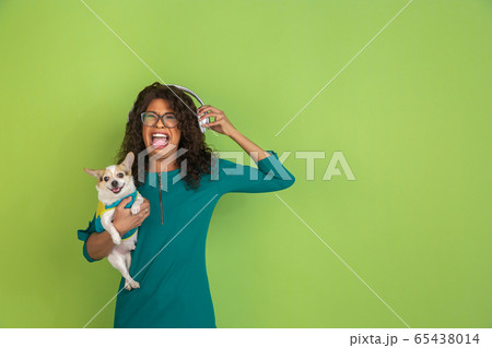 African-american beautiful young woman's portrait with little doggy on green studio background, emotional and expressive. Copyspace for ad. African-american beautiful young woman's portrait with little doggy on green studio background, emotional and expressive. Copyspace for ad. 65438014