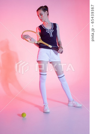 Girl tennis player with a racket in sportswear and white sneakers on a pink background in the Studio with shadow. 65439367