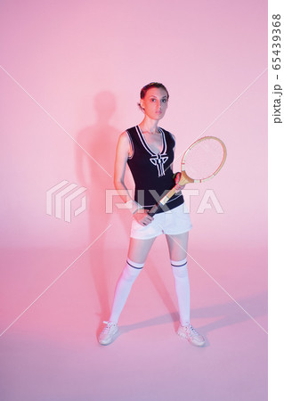 Girl tennis player with a racket in sportswear and white sneakers on a pink background in the Studio with shadow. 65439368