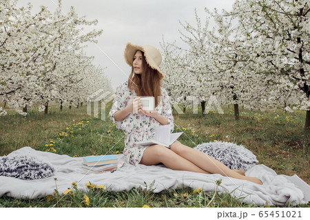 Girl drinking morning coffee in the garden. Woman with a cup of hot drink. Stylish woman in a flower garden. Girl drinking morning coffee in the garden. Woman with a cup of hot drink. Stylish woman in a flower garden. 65451021