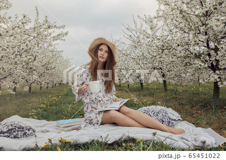 Girl drinking morning coffee in the garden. Woman with a cup of hot drink. Stylish woman in a flower garden. Girl drinking morning coffee in the garden. Woman with a cup of hot drink. Stylish woman in a flower garden. 65451022