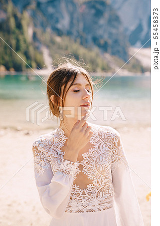 Beautiful bride in a white chiffon dress with sleeves and lace on the shore of Lake Lago di Braies in Italy. Destination wedding in Europe, on the popular Braies lake. 65458373