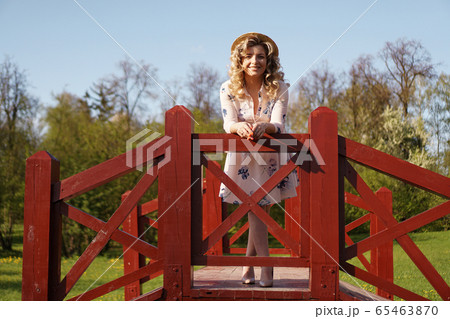 Beautiful woman in summer dress and straw hat stands on birch bridge in the park 65463870