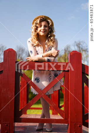 Beautiful woman in summer dress and straw hat stands on birch bridge in the park Beautiful woman in summer dress and straw hat stands on birch bridge in the park 65463871