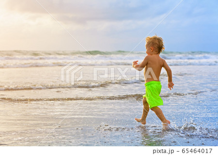 Child run with splashes by water pool along sea 65464017