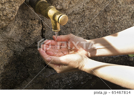 woman's hands picking water from a fountain spout 65467814