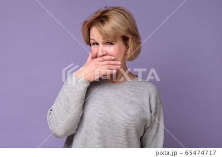 woman with puzzled look covering her mouth trying woman with puzzled look covering her mouth trying 65474717