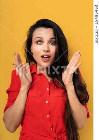 Pretty surprised woman smiling with open mouth and open palms, mixed race brunette with dark hair in red blouse cut out on yellow background. Emotion concept. Sale concept Pretty surprised woman smiling with open mouth and open palms, mixed race brunette with dark hair in red blouse cut out on yellow background. Emotion concept. Sale concept 65480493