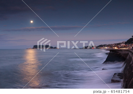 七里ガ浜駐車場から眺める月の光を浴びて輝く海面と江ノ島、朝焼けの空 65481754