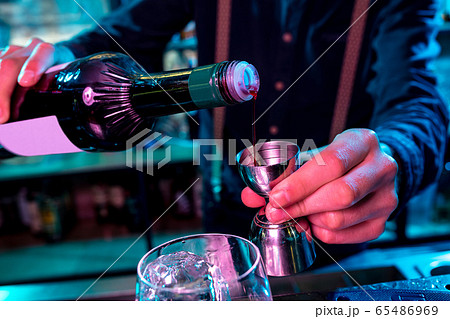 Close up of barman preparing of alcoholic cocktail with shot in multicolored neon light Close up of barman preparing of alcoholic cocktail with shot in multicolored neon light 65486969