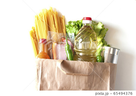 Contactless food delivery, donation essentials. Oil, pasta, salad,chilli,canned food, bacon,spicy sauce. Products in paper bag close up white background Contactless food delivery, donation essentials. Oil, pasta, salad,chilli,canned food, bacon,spicy sauce. Products in paper bag close up white background 65494376