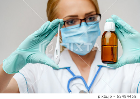 medical doctor nurse woman wearing protective mask and rubber or latex gloves - holding can of medicine and thermometer medical doctor nurse woman wearing protective mask and rubber or latex gloves - holding can of medicine and thermometer 65494458