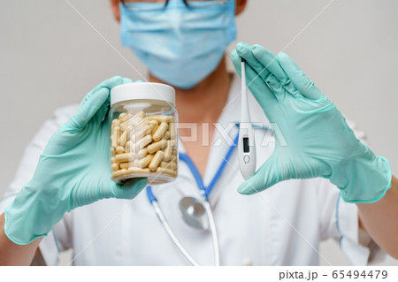 medical doctor nurse woman wearing protective mask and rubber or latex gloves - holding can of medicine and thermometer 65494479