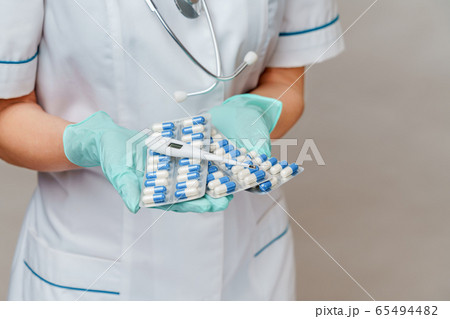 medical doctor nurse woman wearing protective mask and rubber or latex gloves - holding blisters of pills and thermometer medical doctor nurse woman wearing protective mask and rubber or latex gloves - holding blisters of pills and thermometer 65494482