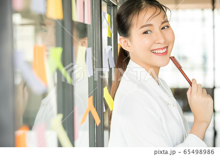 若い きれい 女性 会社員 笑顔 付箋 窓 貼る メモ ペン 人物 素材の写真素材