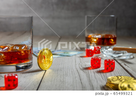 Two Glasses With Whiskey, Bitcoins and Dice on a Rustic Wooden Table 65499321