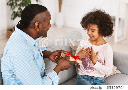 Celebrating birthday at home. African American granddad congratulating his grandchild with present indoors 65529704