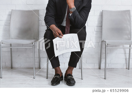 Closeup view of black guy in office suit with resume waiting for job interview at company foyer 65529906