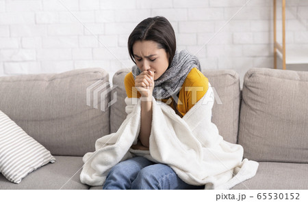 Sick young lady suffering from virus, coughing into her hand at home 65530152