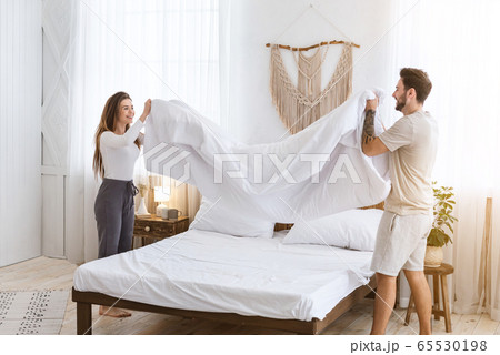 Couple making a bed together. Man and woman holding blanket in bedroom 65530198