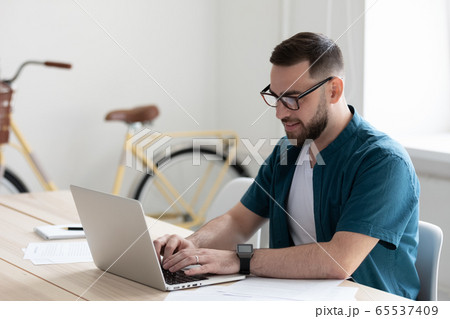 Happy young confident bearded businessman typing on keyboard using laptop. 65537409