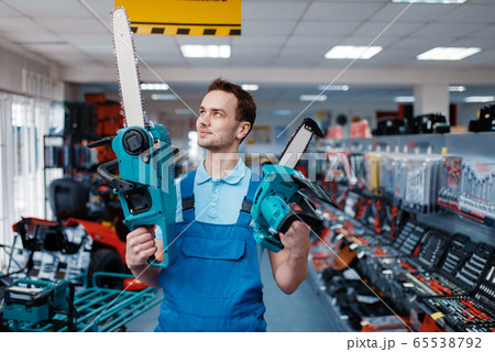 Worker holds big and small chainsaws in tool store Worker holds big and small chainsaws in tool store 65538792