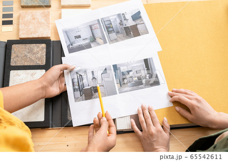 Overview of hands of two young female designers of interior discussing photos 65542611