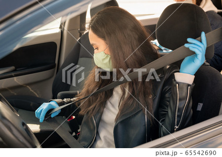 Young brunette female in leather jacket, gloves and mask fastening seatbelt 65542690