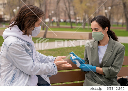 Young female in protective gloves and mask spraying sanitizer on hands of man Young female in protective gloves and mask spraying sanitizer on hands of man 65542862