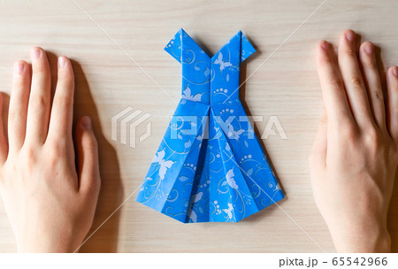 Girl's hands making origami blue dress from butterfly printed paper. Step by step instruction, step17. Mother's day, birhday, summer gift, family leisure time concept. DIY tutorial, flatlay, top view Girl's hands making origami blue dress from butterfly printed paper. Step by step instruction, step17. Mother's day, birhday, summer gift, family leisure time concept. DIY tutorial, flatlay, top view 65542966
