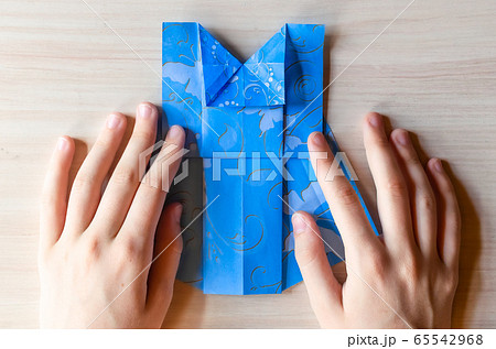Girl's hands making origami blue dress from butterfly printed paper. Step by step instruction, step15. Mother's day, birhday, summer gift, family leisure time concept. DIY tutorial, flatlay, top view Girl's hands making origami blue dress from butterfly printed paper. Step by step instruction, step15. Mother's day, birhday, summer gift, family leisure time concept. DIY tutorial, flatlay, top view 65542968