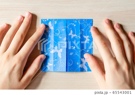 Girl's hands making origami blue dress from butterfly printed paper. Step by step instruction, step10. Mother's day, birhday, summer gift, family leisure time concept. DIY tutorial, flatlay, top view 65543001