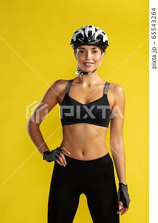 Confident female cycler. Young sporty woman in biking helmet keeping arm on hip and looking at camera while standing against yellow background. Studio shot 65543264