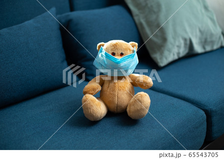 Cute teddy bear on the blue sofa with protective mask on him Cute teddy bear on the blue sofa with protective mask on him 65543705
