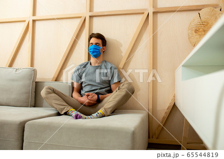 Young man in blue mask sitting on sofa in room Young man in blue mask sitting on sofa in room 65544819