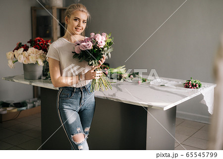 Smiling young woman wearing fashion clothes holding bouquet of flowers 65545799