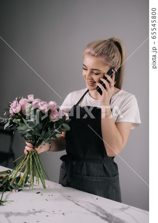 Professional young woman florist wearing apron talking on mobile phone with client 65545800